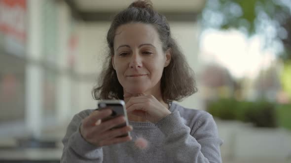 Smiling Middle Aged Woman Using Smartphone on Street.