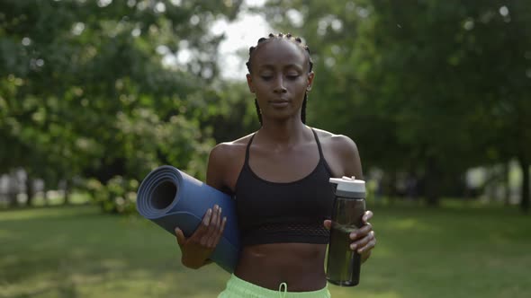 Sporty Woman with Braids Carrying Water Bottle and Yoga Mat
