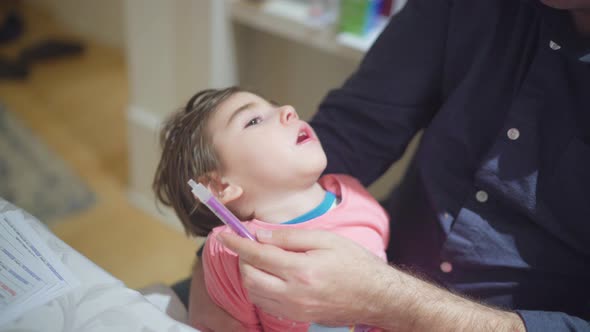 A father is feeding his little girl with cerebral palsy special need in his arms with syringe at hom