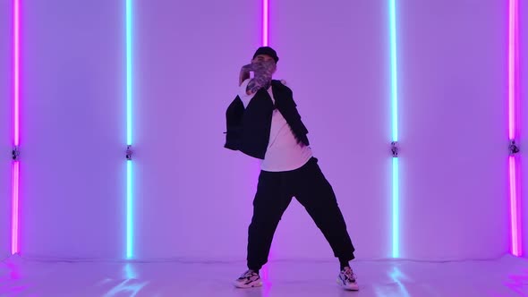 Young Man with Tattoos Dressed in Stylish Youth Clothes and a Cap Dancing in Hip Hop Style