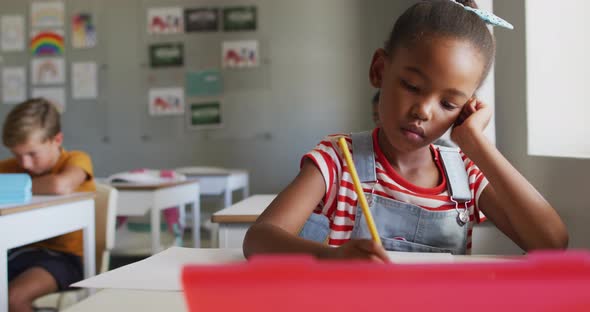 Video of thoughtful african american girl sitting at desk in classroom alt