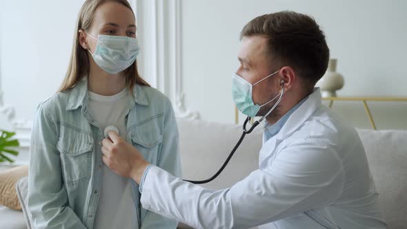 Male Doctor Listens to the Heart and Lungs of a Female Patient While Sitting on the Couch