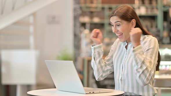 Beautiful Young Latin Woman Celebrating Success on Laptop in Cafe 