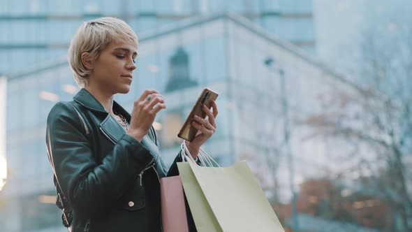 Young Short Haired Woman with Shopping Bags Using Smartphone in Front of Shopping Mall