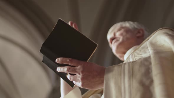 Caucasian Old Clergyman Reading Holy Bible in Church