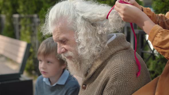 Close-up Side View of Senior Caucasian Bearded Retiree Sitting on Bench with Grandchildren and