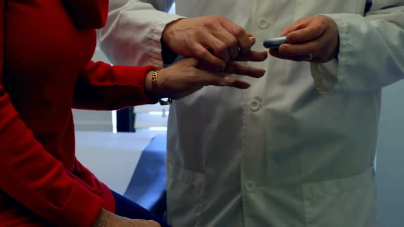 Mid section of young Asian male doctor measuring blood sugar level with glucometer of senior woman i