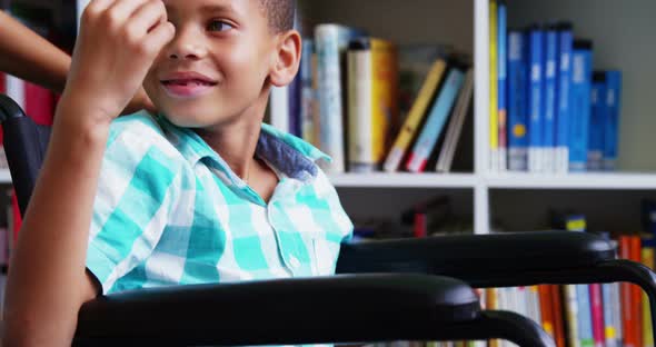 Happy schoolboy carrying his friend in wheelchair at library