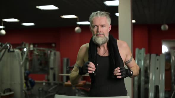 Slow motion of jogging gray-haired adult man on treadmill in gym