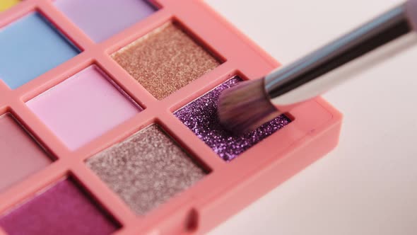 Make-up artist picks up purple shimmer pigment from bright colorful eyeshadow palette