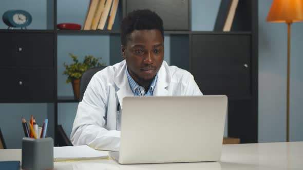 African Doctor Discussing and Consulting Patient About Symptoms Online on Laptop at Hospital Office