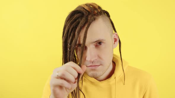 Young Man Twisting Hair and Looking at Camera on Yellow Background