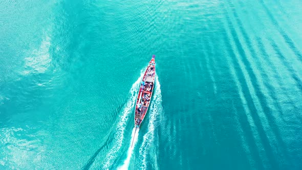 Long-tail boat sailing on vibrant turquoise water, tracing sea surface reflecting sunlight in Thaila