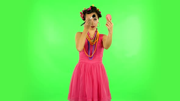 Girl with Curlers on Her Head in a Pink Dress Looking in Red Mirror and Powdered Her Nose