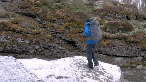 Tourist with a Backpack Climbs a Rock By a Mountain River. Active Adventures and Travel