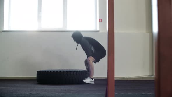 Side View of Athletic Man Flipping Tyre During Workout in Gym