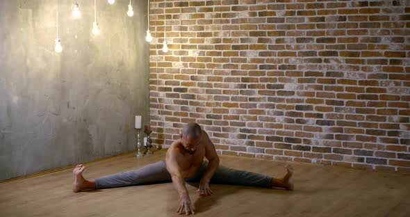 Muscular Man Is Stretching Legs Sitting in a Split on Floor in Home in Evening