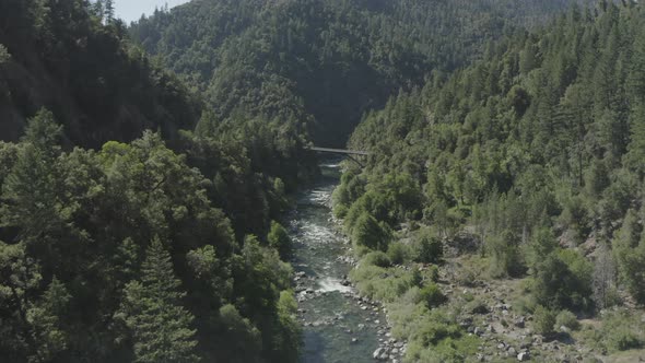 Slow forward drone flight over a rocky river toward a tall bridge