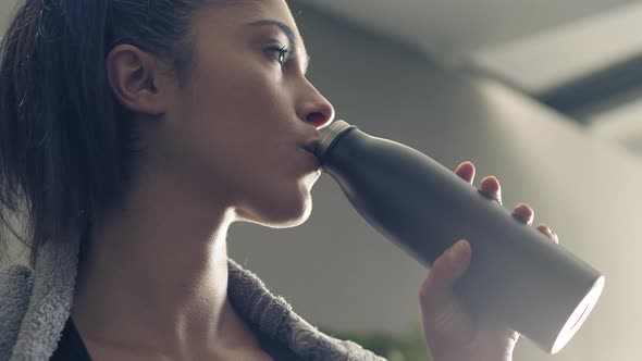 Fitness Woman Drinking From Sport Bottle During a Workout Pause at Home or Gym. Close Backlit