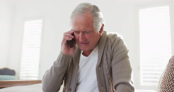 Cheerful retired senior man talking on mobile phone while sitting at home