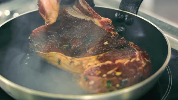 The Cook Puts a Large Piece of Juicy Steak on a Hot Pan and Begins to Fry It in Oil Closeup