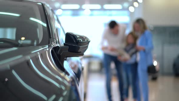 Shiny Luxurious New Car in Dealership with Blurred Parents and Daughter Examining Specifications at