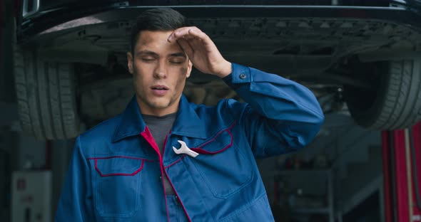 Portrait of Dirty Exhausted Auto Service Worker, Tired After Car Repair, Wiping His Forehead