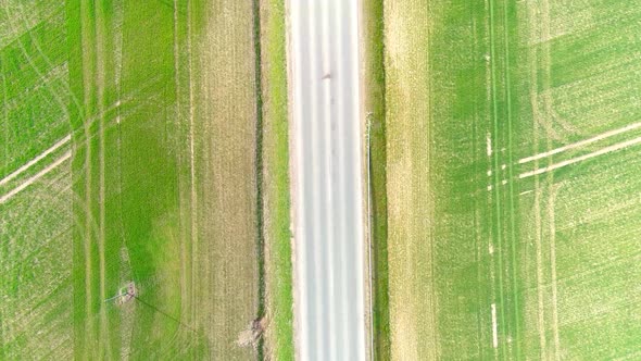 aerial drone view of rural road with cars moving from right to left in the form of green fields in L
