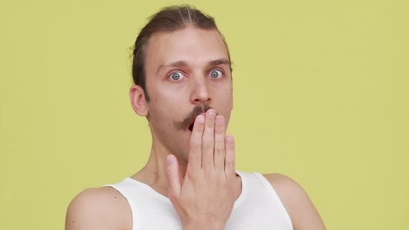 Closeup Astonished Young Man Closing His Mouth with Hand in Surprise Over Yellow Background Slomo