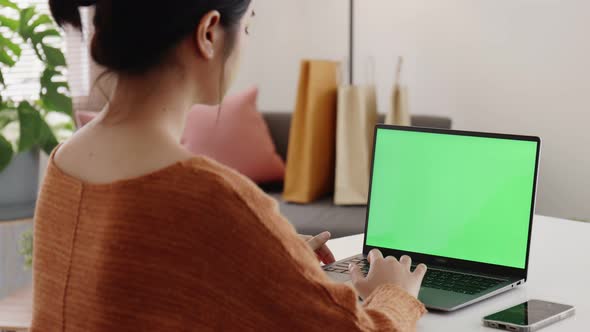 Young Asian woman using laptop computer at home with green blank monitor screen.