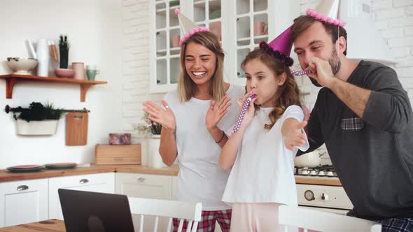 Happy Family with a Daughter Celebrating Birthday in Kitchen Using Laptop for a Video Call During