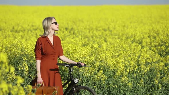 girl in vintage dress and sunglasses with bicycle in rapeseed field