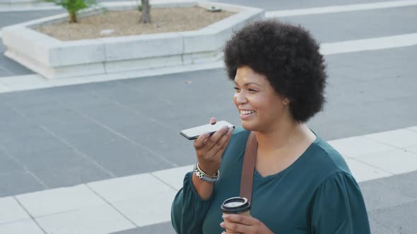 Happy plus size biracial woman talking on smartphone and drinking coffee