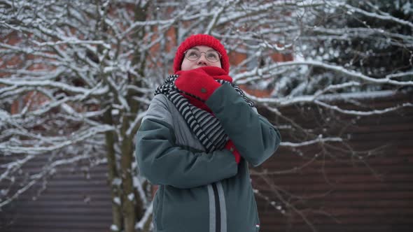 Young woman shrinks from cold and wraps herself tighter in a scarf in the cold