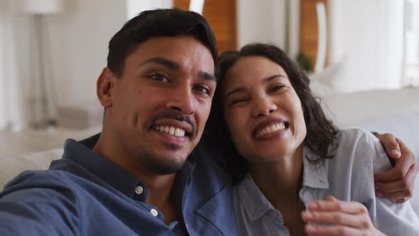 Romantic hispanic couple embracing sending kisses on sofa in living room