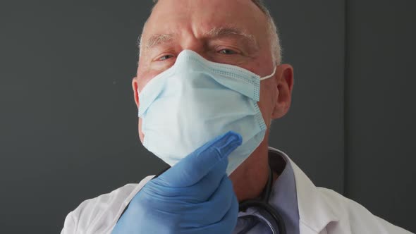 Portrait of caucasian senior male doctor lowering his face mask and smiling