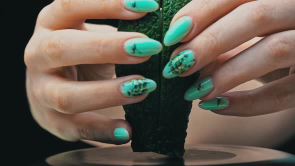 Girl's Hand Holds an Avocado Cut Into Two Parts on a Black Background