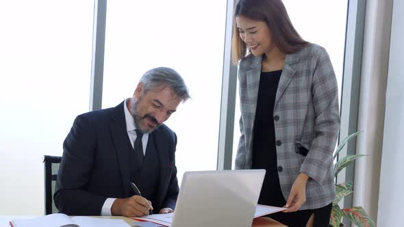 Young asian secretary in suit asking senior Caucasian boss to sign agreement