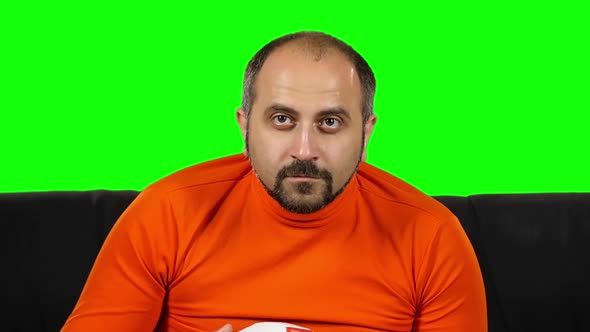 Male Football Fan Sitting on Sofa and Watching Soccer with Ball in His Hands. Green Screen. Slow
