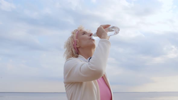 Senior Woman Drinking Water After Exercising on Summer Beach