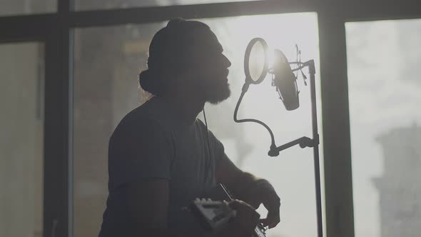 A Young Musician with a Guitar Sings in Front of a Wireless Studio Microphone