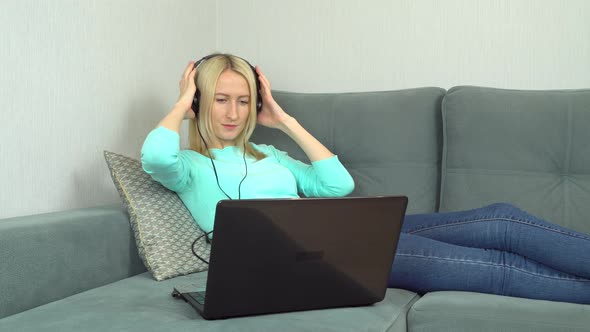a Beautiful Young Woman Listens to Music at Home Using Headphones and a Laptop