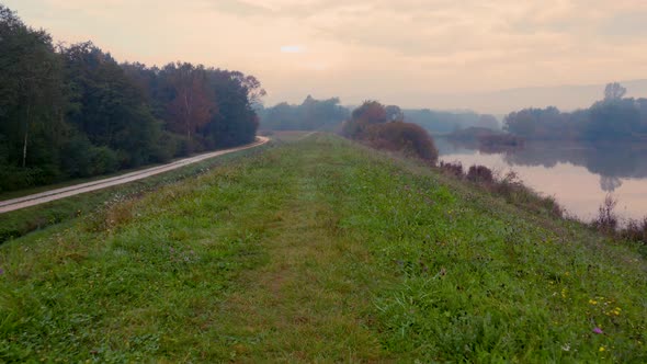 Path with lake view and a single road bordering it at foggy autumn morning in Central Europe. Low ae