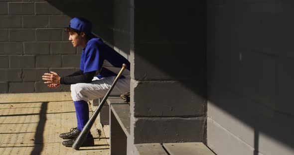 Nervous mixed race female baseball player, sitting on bench in sun waiting with baseball bal