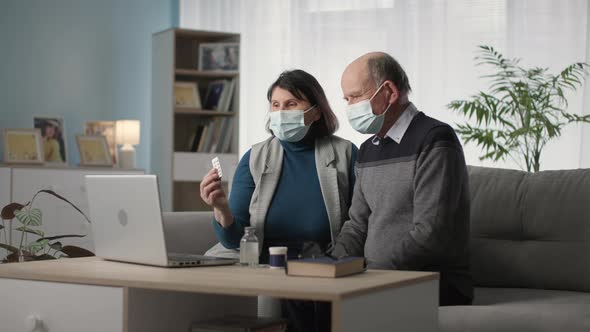Modern Elderly Man and Woman in Medical Masks Communicate By Video Call with Family Doctor About