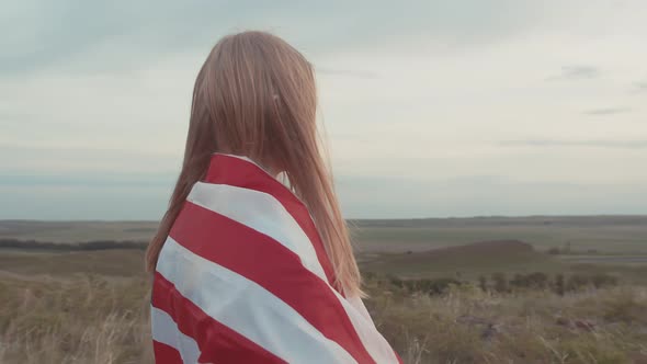 Woman Put Flag America on Shoulders and Stands in Field Watching Sunset