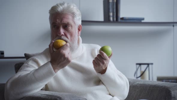 Elderly Man with a Gray Beard Sniffs Lemon and Apple and Does Not Smell