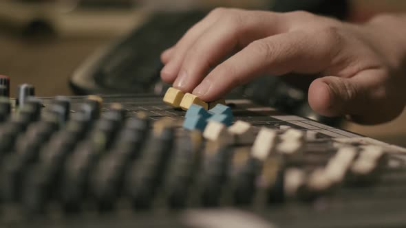 Mens hand pulling up knobs of audio mixer in studio