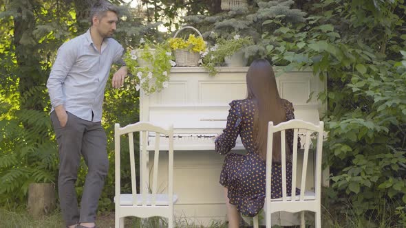 Wide Shot of Happy Mid-adult Man Standing Next To Piano and Listening To Brunette Woman Playing