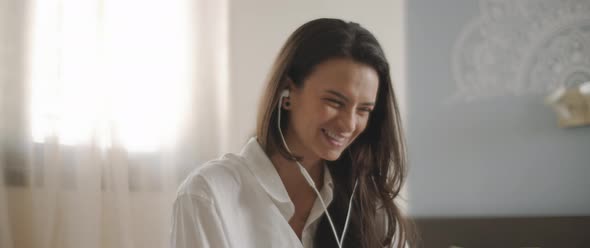 Close up of a young woman talking to someone through earphones while sitting on bed. 